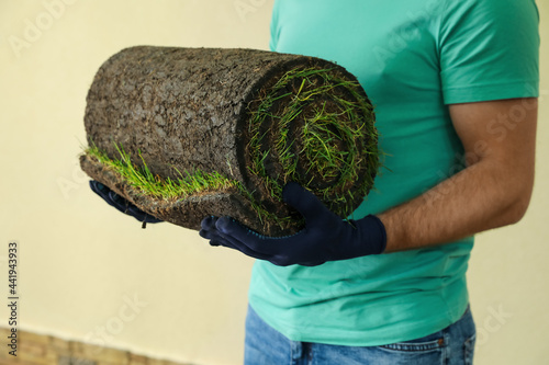 Young man holding rolled grass sod at backyard, closeup