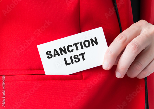 SANCTION LIST is written on a white map in the hands of a businessman, puts the card in his jacket pocket