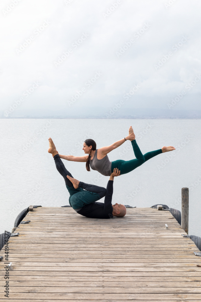 Couple practicing acroyoga on a dock on a lake