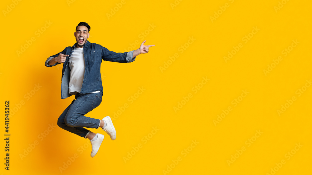 Emotional arab guy jumping up and pointing at copy space