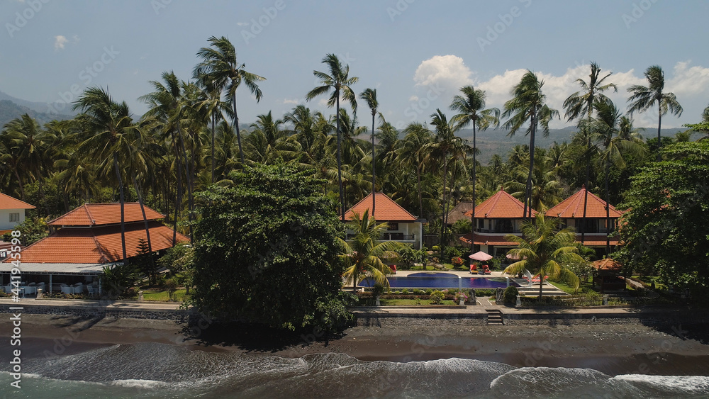 aerial view luxury hotel with swimming pool, sun beds, palm trees by sea. seascape coastline with black sand beach, palm trees, hotel, tropical resort. Bali,Indonesia, travel concept.