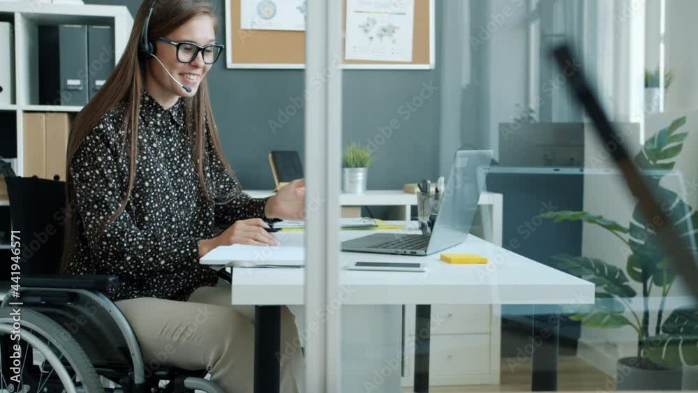 Cheerful handicapped girl employee is talking to clients online with ...