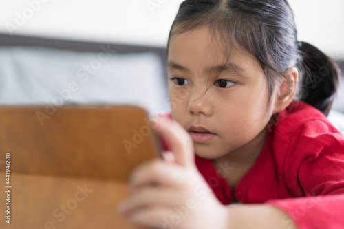 Asian child or kid girl enjoy learn from home or people study online on computer tablet to e-learning communication with happy playing and sleep lying watching pad on bed in room by back to school