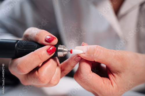 Home manicure. In the photo  female hands with red nails hold a nail cutter  machine  for manicure. The photo shows the process of removing old gel polish.
