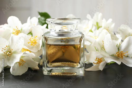 Jasmine essential oil and fresh flowers on dark grey table