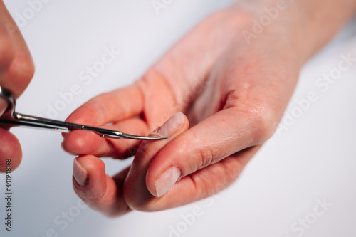 Home manicure. In the photo  a woman cuts off a raised cuticle with manicure scissors.