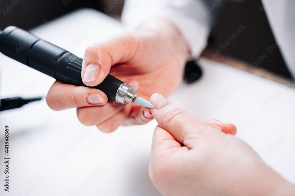 Fototapeta premium Home manicure. In the photo, a woman removes the top layer of the nail plate using a nail cutter.