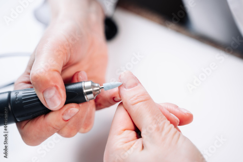 Home manicure. In the photo  a woman removes the top layer of the nail plate using a nail cutter.