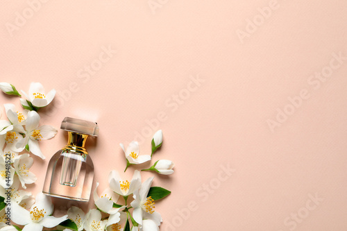 Bottle of luxury perfume and fresh jasmine flowers on beige background, flat lay. Space for text