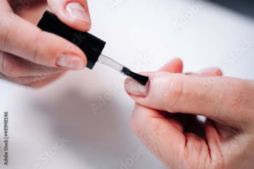 Home manicure. In the photo, a woman applies a beige gel polish (coating, base) with a brush for further drying under a manicure lamp.