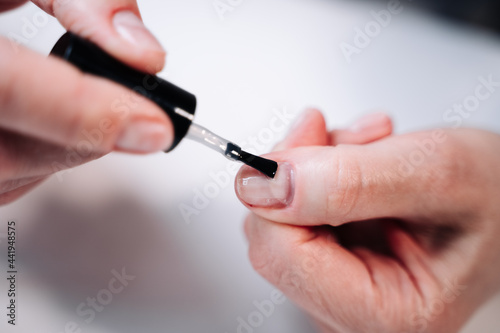 Home manicure. In the photo  a woman applies a beige gel polish  coating  base  with a brush for further drying under a manicure lamp.