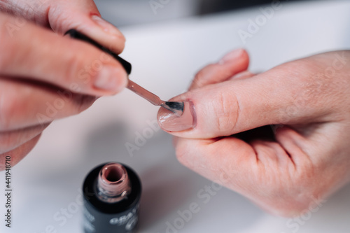 Home manicure. In the photo  a woman applies a beige gel polish  coating  base  with a brush for further drying under a manicure lamp.