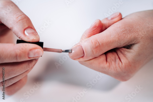 Home manicure. In the photo  a woman applies a beige gel polish  coating  base  with a brush for further drying under a manicure lamp.