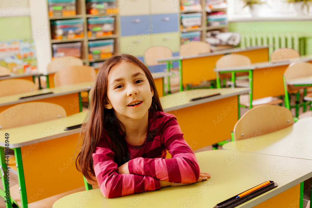 The joyful schoolgirl is sitting at a desk in the classroom The joyful schoolgirl is sitting at a desk in the classroom