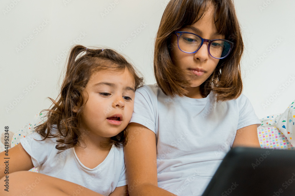 Two girls sitting on their beds with a tablet. Two girls sitting on their beds with a tablet.
