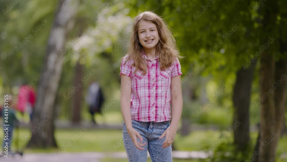 Portrait of schoolgirl child in a summer park. Kid looks into camera, smiles and waves her hands Portrait of schoolgirl child in a summer park. Kid looks into camera, smiles and waves her hands