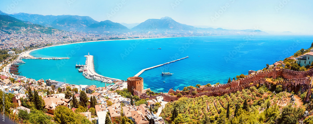 Beautiful panoramic image of bay of resort town of Alanya with symbol of city - Red Tower, ancient fortress walls, turquoise sea, chain of mountains on horizon.