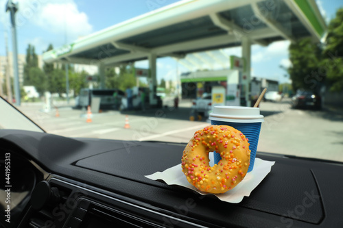 Fototapeta Naklejka Na Ścianę i Meble -  Paper coffee cup and doughnut on car dashboard at gas station