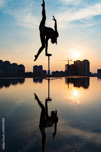 Silhouette of flexible acrobat doing handstand on the dramatic sunset and cityscape background. Concept of individuality  creativity and outstanding