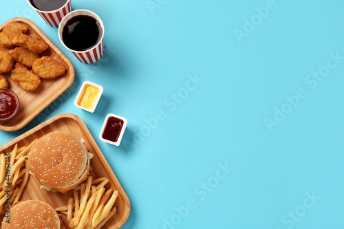 Different fast food on turquoise background, flat lay. Space for text