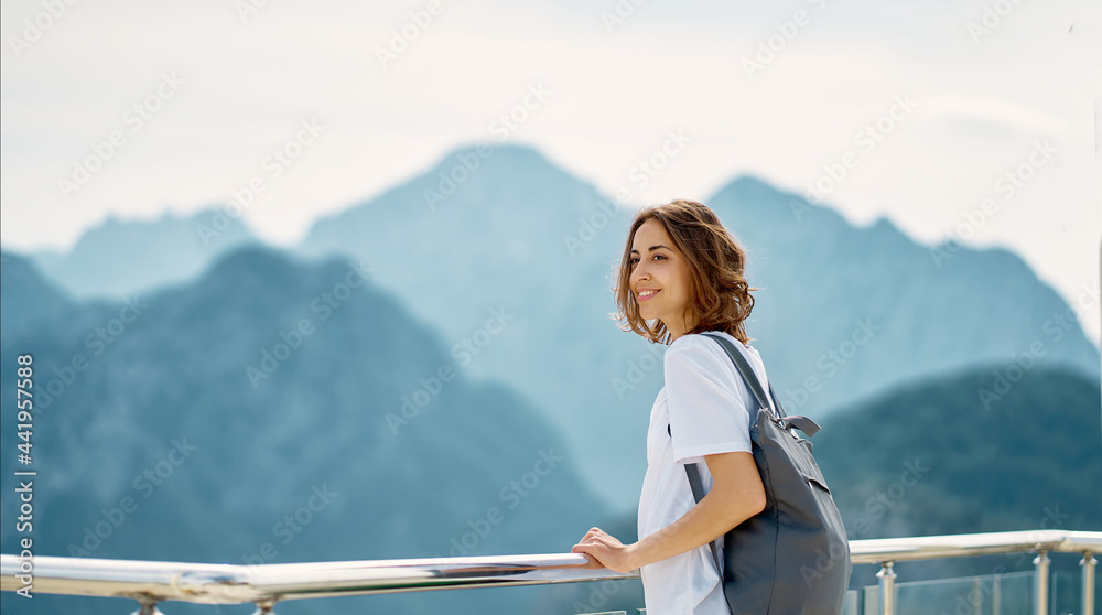 Cheerful tourist woman with backpack standing by railing on mountain top, enjoying viewpoint of Tunektepe Teleferik, Antalya