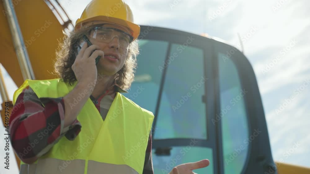 Excavator operator in hard hat talking by smartphone.