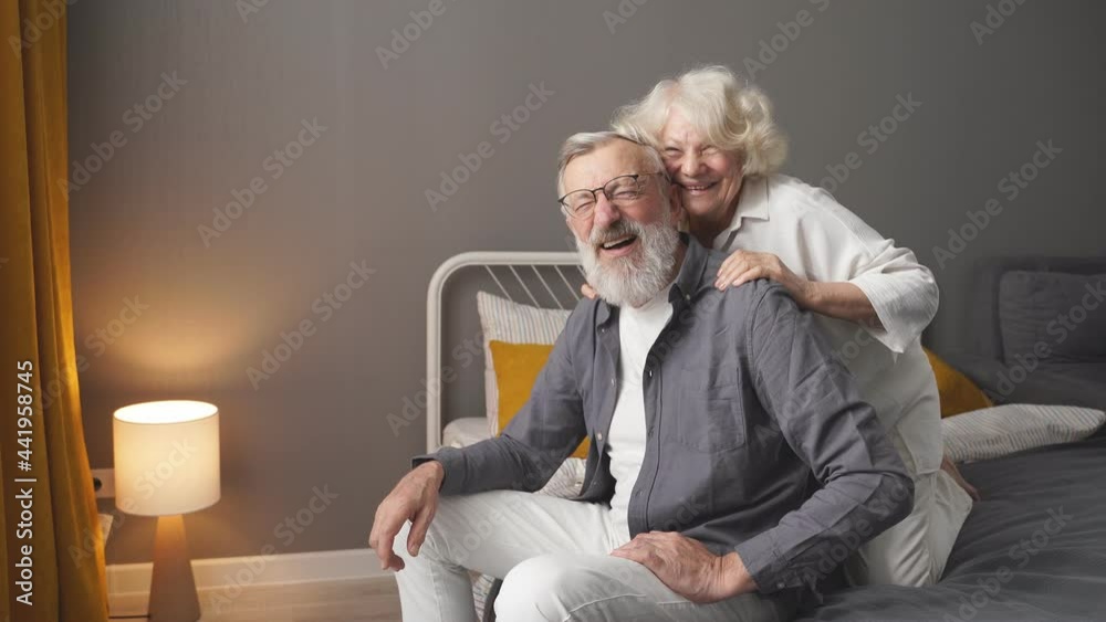 Portrait of happy retired couple sitting at home in bedroom, smiling, having fun, spend weekend together. Portrait of happy retired couple sitting at home in bedroom, smiling, having fun, spend weekend together.