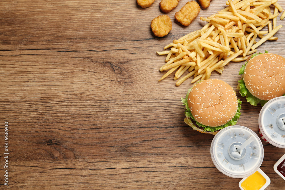 Flat lay composition with delicious fast food menu on wooden table. Space for text