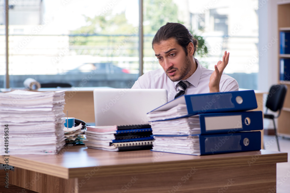Young male employee unhappy with excessive work in the office Young male employee unhappy with excessive work in the office