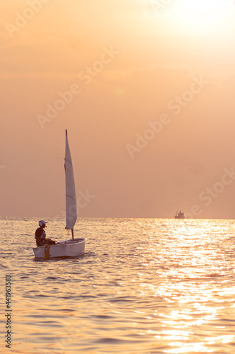 Handsome young boy learning to sail a sailing boat at sunset in the ocean