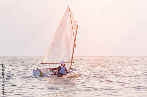 Handsome young boy learning to sail a sailing boat at sunset in the ocean