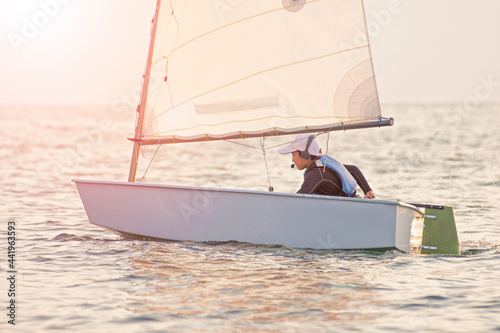 Handsome young boy learning to sail a sailing boat at sunset in the ocean