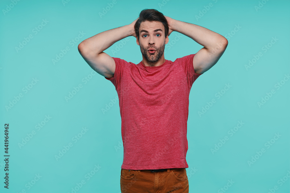 Fototapeta premium Excited young man in casual clothing looking at camera and holding hands on head