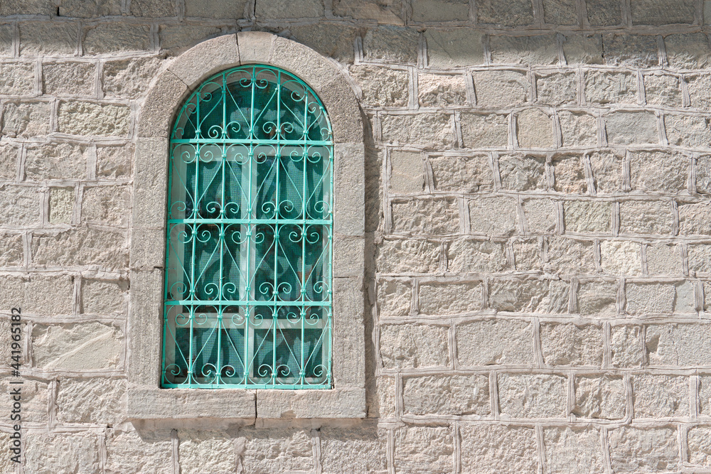 Green window with wrought iron grating and stone wall