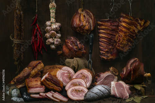 Smoked pork sausage, back ribs, pork neck, breast and knuckle. Traditional various smoked meats, vegetales and rye bread on a wooden table with background