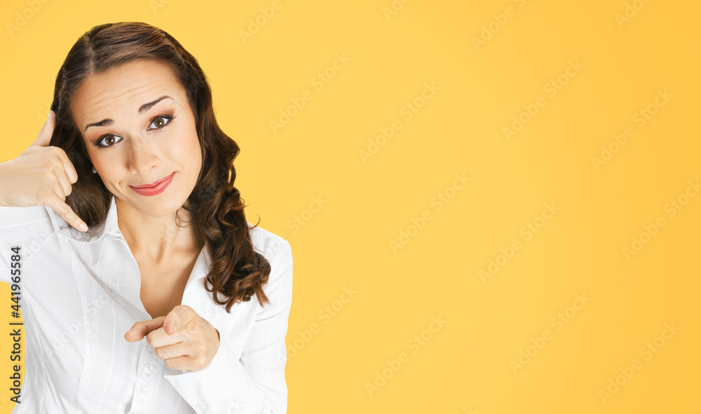 Image of businesswoman in white confident clothing showing call me gesture and pointing at viewer, orange yellow colour background. Smiling brunette woman at studio. Business helpline center concept. Image of businesswoman in white confident clothing showing call me gesture and pointing at viewer, orange yellow colour background. Smiling brunette woman at studio. Business helpline center concept.