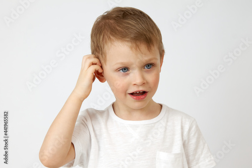A little boy with blue eyes is deep in thought and scratching his head on a white background. Solving a difficult task by a child