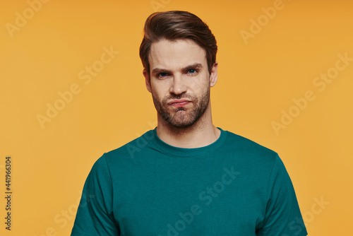 Portrait of frustrated young man looking at camera while standing against yellow background © gstockstudio