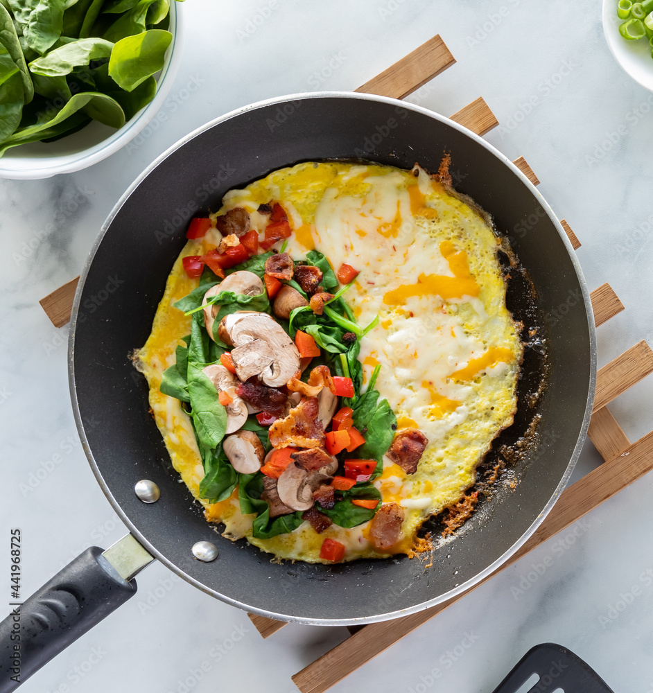 Top down look into a fry pan with the ingredients of the inside of an omelette right before folding. Top down look into a fry pan with the ingredients of the inside of an omelette right before folding.