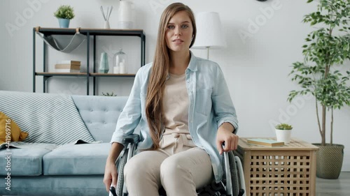 Portrait of young lady in wheelchair wearing casual clothing sitting at home alone and looking at camera. Physical disability and health problems concept. photo