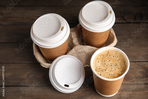 Takeaway paper coffee cups with plastic lids and cardboard holder on wooden table