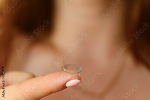 The girl holds the lens on her finger in front of her to put it on