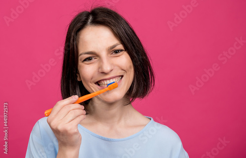 Beautiful happy young woman with toothbrush on blank pink background