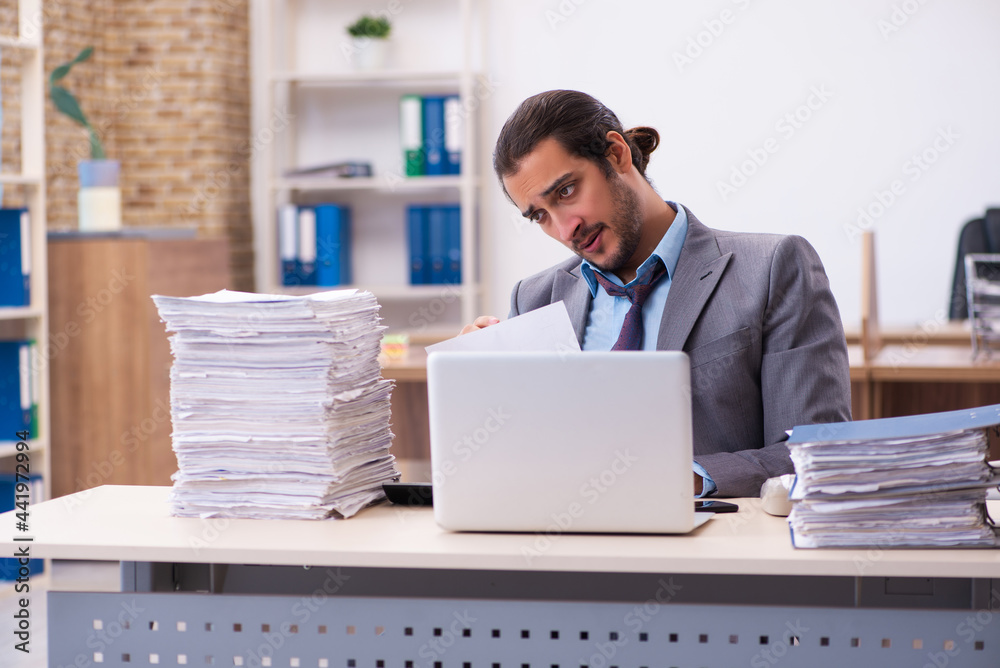 Young male employee unhappy with excessive work in the office Young male employee unhappy with excessive work in the office