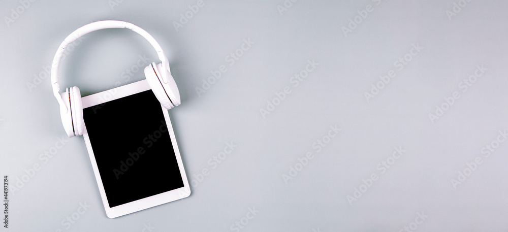 Digital tablet with wireless headphones on gray background. Online learning, remote education, e-learning, technology concept Digital tablet with wireless headphones on gray background. Online learning, remote education, e-learning, technology concept