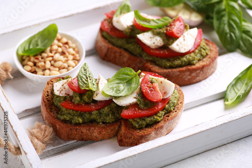 Italian cuisine. Rustic. Bruschetta with pesto sauce, fresh tomatoes, mozzarella and basil on a wooden board on a white table with pine nuts in bowl. Background image, copy space