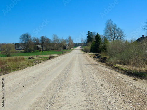 Country road made of loose white stones going straight in the distance in Latvia  sunny day in early spring
