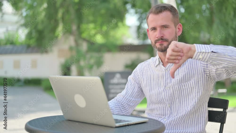 Thumbs Down by Middle Aged Man with Laptop in Outdoor Cafe Thumbs Down by Middle Aged Man with Laptop in Outdoor Cafe