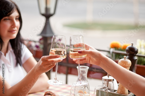 Women holding the glasses of white wine making a toast. Woman cheers.