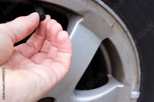 The fingers of a woman's hand unscrew the valve on a car tire 